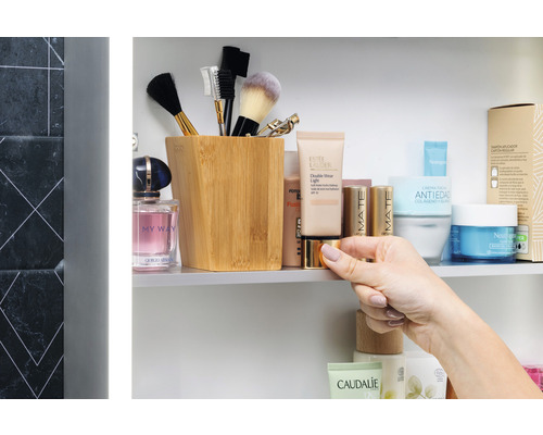 Badkamerscène met cosmetische producten, make-upborstels en een houten bakje in een spiegelkast.