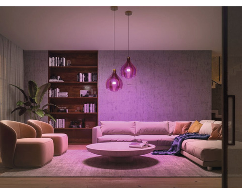 Lichte woonkamer met bank, fauteuils, salontafel, boekenkast en twee hanglampen voor een gezellige sfeer.