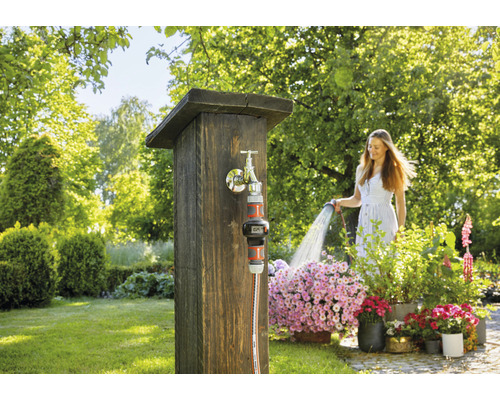 Vrouw besproeit bloemen met een tuinslang bij een kraan in de tuin