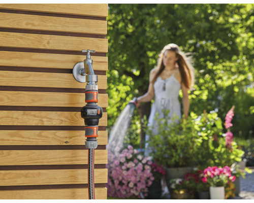 Tuinwatermeter op waterkraan met vrouw op de achtergrond die de tuin besproeit