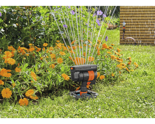 Tuinscene met gazonsproeier in actie om bloemen te besproeien