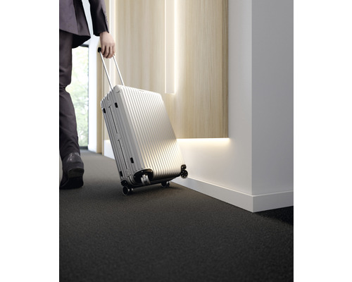 Persoon trekt zilverkleurige rolkoffer over tapijt