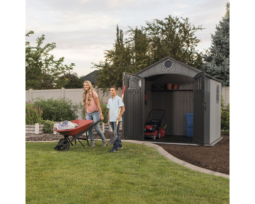Tuinscène met een tuinhuis, een kruiwagen en twee mensen die tuinieren