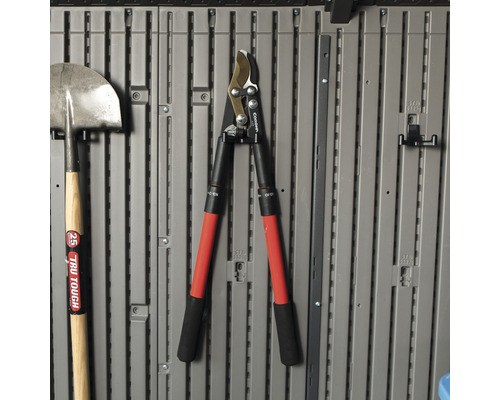 Tuin gereedschap zoals een spade en heggenschaar hangen aan een grijze muur