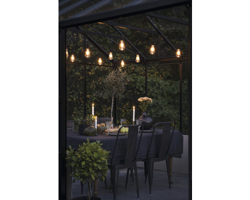 Eettafel met stoelen, kaarsen en verlichting in een kas