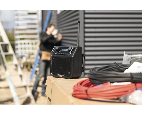 Bouwradio met antenne en kabels op een bouwplaats met een bouwvakker op de achtergrond