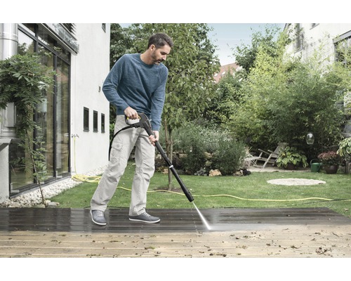 Man reinigt een houten terras met een hogedrukreiniger in een tuin.