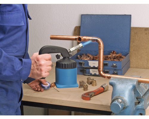 Man soldeert koperen buizen met een soldeerbrander, fittingen en gereedschap op een werkbank