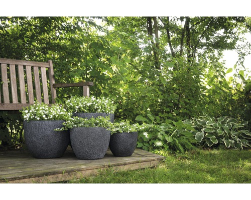 Drie beplante, donkere plantenbakken van kunststof op een houten terras in een tuin.