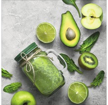 Groene smoothie in een glazen pot met deksel, omringd door limoenen, avocado, appel, kiwi en spinazie.