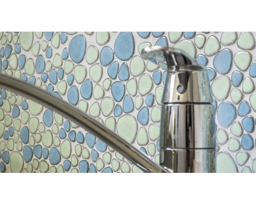 Close-up van een waterkraan voor een wand met mozaïektegels in kiezelpatroon