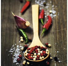 Houten lepel gevuld met peperkorrels, teentje knoflook en chilipepers op een tafel.