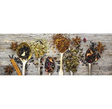 Diverse theesoorten in lepels met steranijs en kaneelstokje op een houten achtergrond.