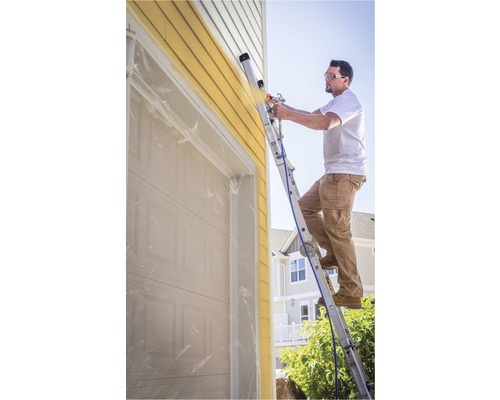 Man op ladder schildert huisgevel met verfspuit