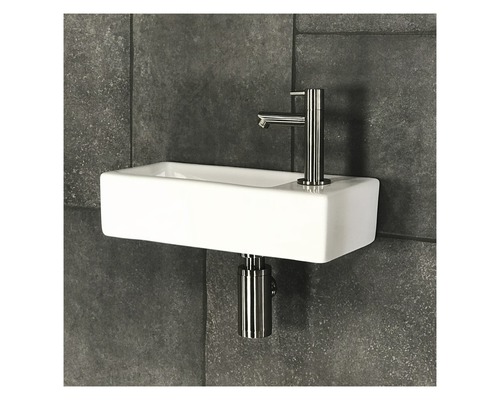 Keramische wastafel met kraan en sifon tegen een donkere tegelachtergrond