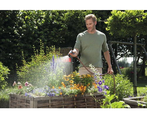 Man besproeit bloemen in een verhoogde tuinbak met een tuinslang