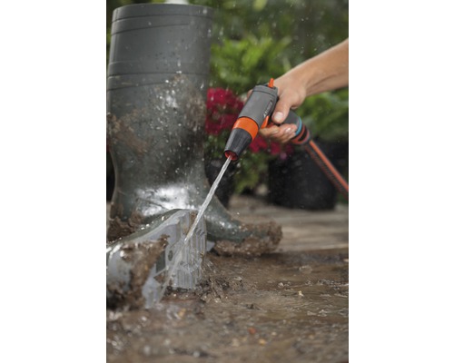 Een persoon reinigt een tuinschep met een tuindouche naast rubberlaarzen.
