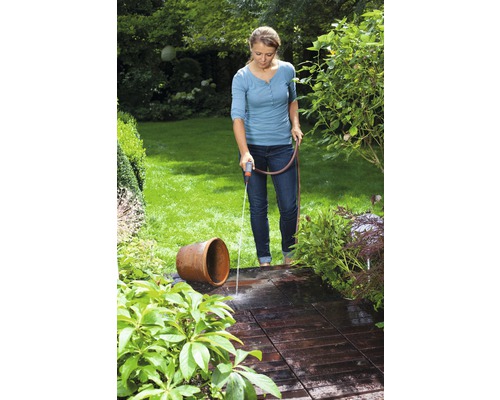 Vrouw sproeit met een tuinslang een terras en een bloemenvaas in de tuin.