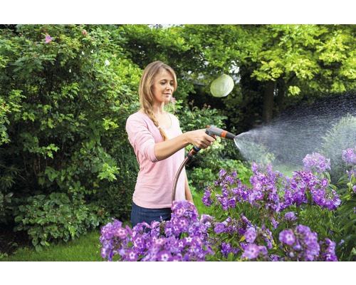 Vrouw besproeit bloemen met een tuinslang in de tuin.