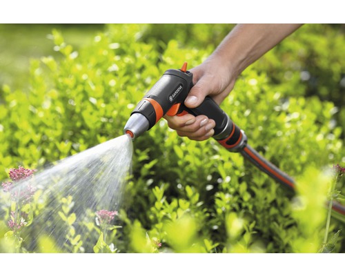 Een hand houdt een Gardena tuinspuit vast, die water op planten spuit.