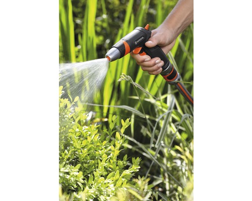 Een hand houdt een tuinspuit vast die water op planten sproeit.