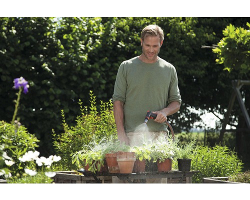 Een man besproeit planten in potten met een tuinslang in de tuin.
