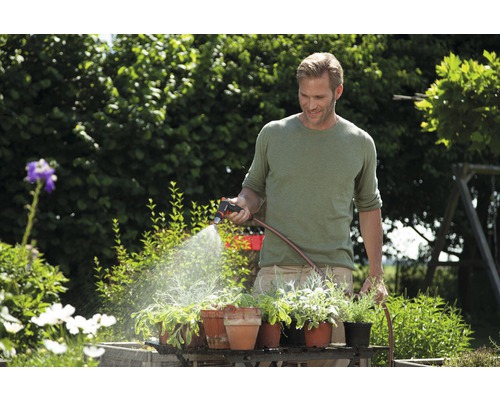 Een man besproeit planten in de tuin met een tuinspuit en een tuinslang.