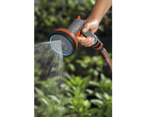 Een persoon houdt een Gardena multifunctionele tuinspuit vast die water sproeit.