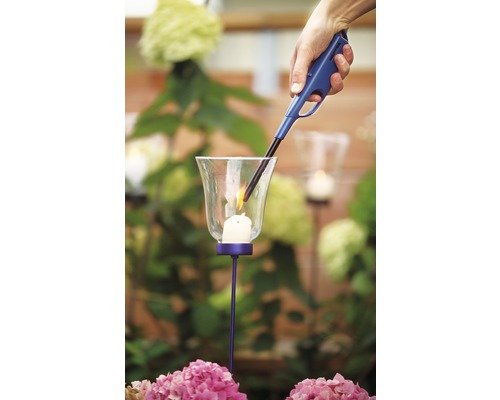 Een hand steekt een kaars in een windlicht aan met een aansteker.