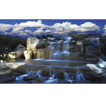 Kunstmatige waterval met rotsen en planten onder een blauwe hemel