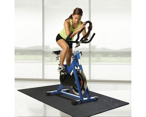 Vrouw traint op een blauwe indoorfiets op een zwarte mat