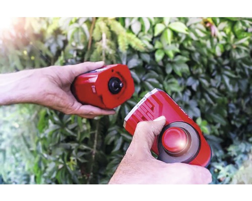 Twee handen houden een elektronische marterverjager vast voor groen loof