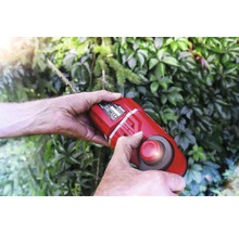 Persoon bedient een accubosmaaier voor een groene haag.