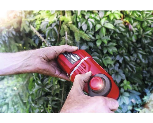 Persoon bedient een accubosmaaier voor een groene haag.