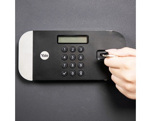 Yale logo. Detail van een kluis met digitaal toetsenbord en een hand die een sleutel invoert.