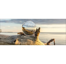 Decoratieve glazen bol op een stuk drijfhout op het strand