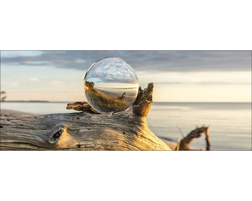Decoratieve glazen bol op een stuk drijfhout op het strand