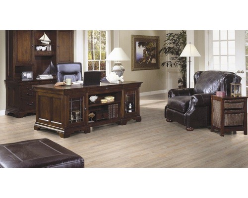 Kantoor met bureau, boekenkast, fauteuil en voetenbank in een lichte ruimte.