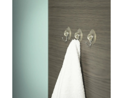 Drie transparante haken met zuignap en een witte handdoek aan een houten wand