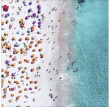 Luchtfoto van een strand met mensen, parasols en blauw water