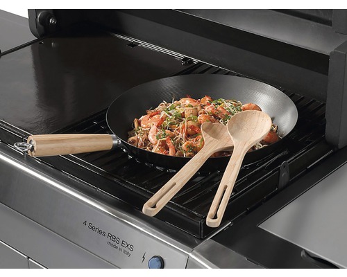 Een gasbarbecue met een wok met garnalen en twee houten lepels.