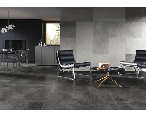 Moderne woonkamer met grijze vloertegels, wandtegels met steenlook en zwarte leren fauteuils.