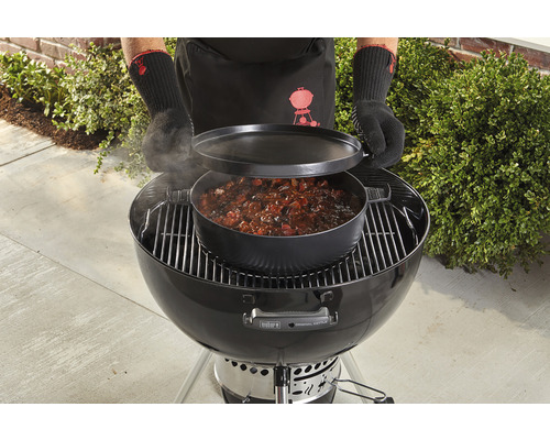 Weber kogelbarbecue met kookpot en deksel, bediend door persoon met barbecuehandschoenen.