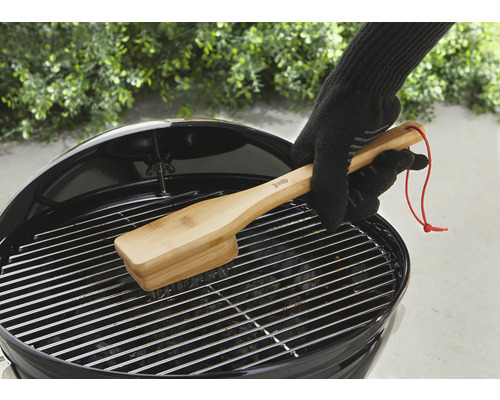 Een persoon reinigt een barbecue rooster met een bamboe barbecueborstel