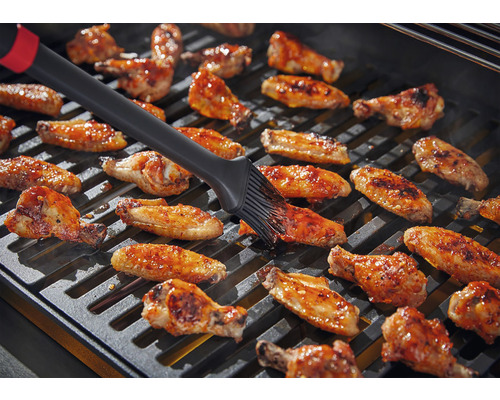Kippenvleugels worden op een grill geborsteld.