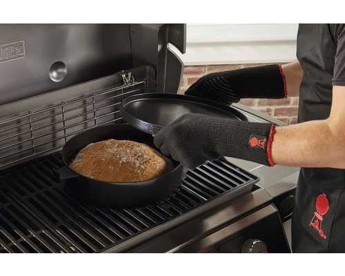 Broodbakken in een Dutch oven op de barbecue met barbecuehandschoenen en schort