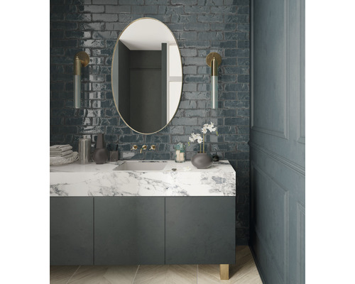 Moderne badkamer met wastafel, spiegel en wandlampen tegen een bakstenen muur.