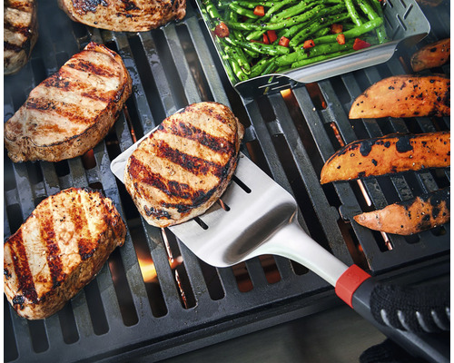 Op een barbecue liggen steaks, zoete aardappelen en groene bonen, waarbij een steak wordt omgedraaid met een barbecuespatel.