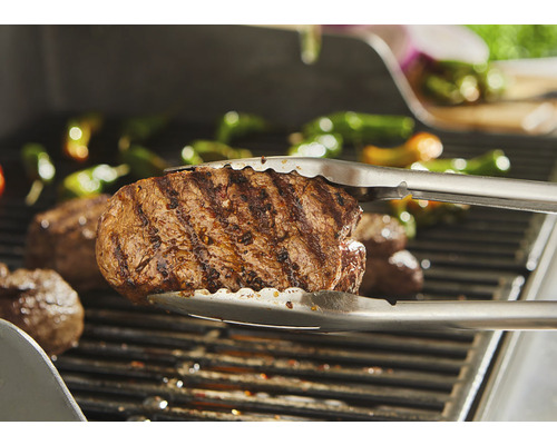 Steaks worden met een grilltang op een barbecue omgedraaid.