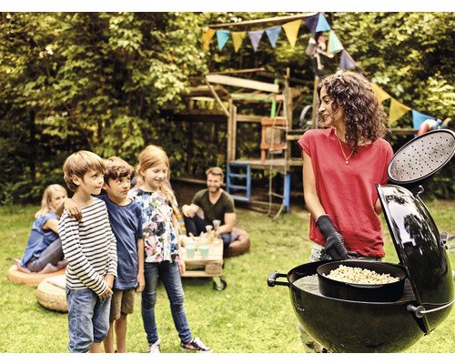 Een vrouw grilt in de tuin met kinderen en een bolvormige barbecue.